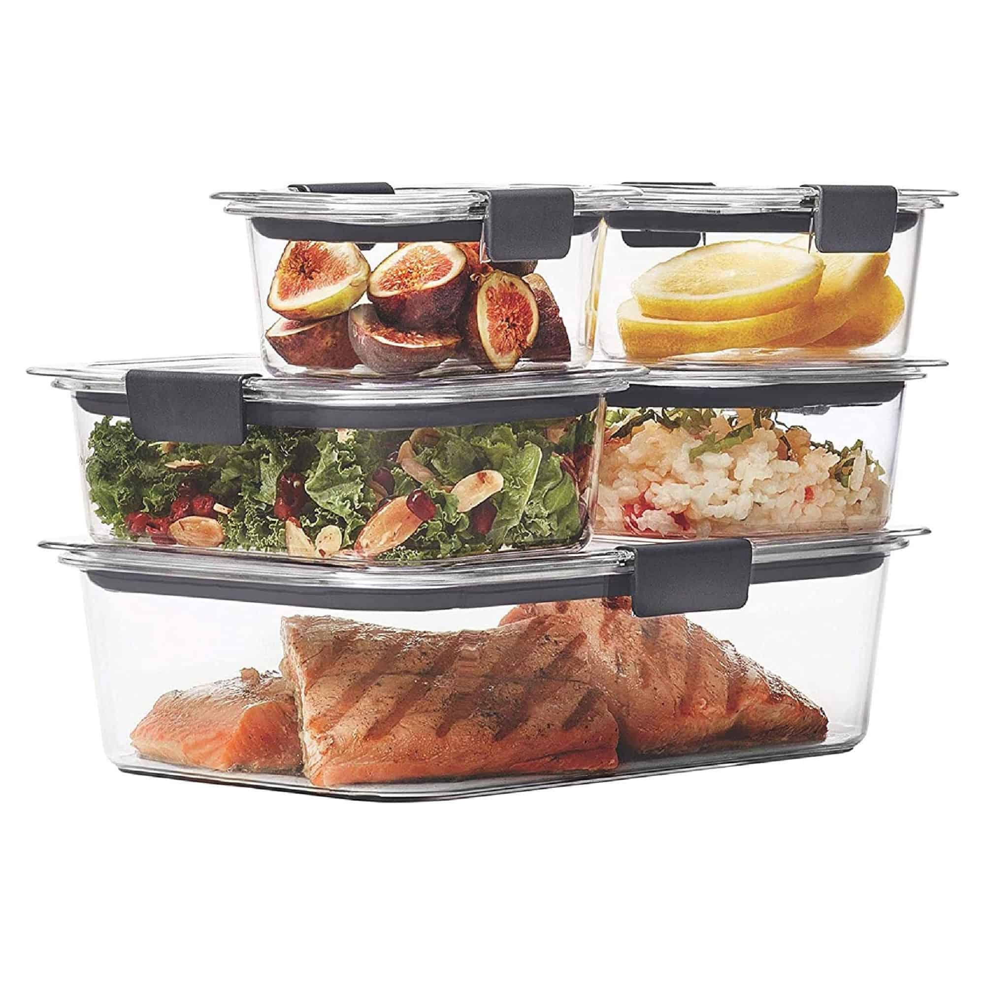 Stacked glass containers with black lids, holding grilled salmon, salad with nuts, rice with vegetables, lemon slices, and fig halves.