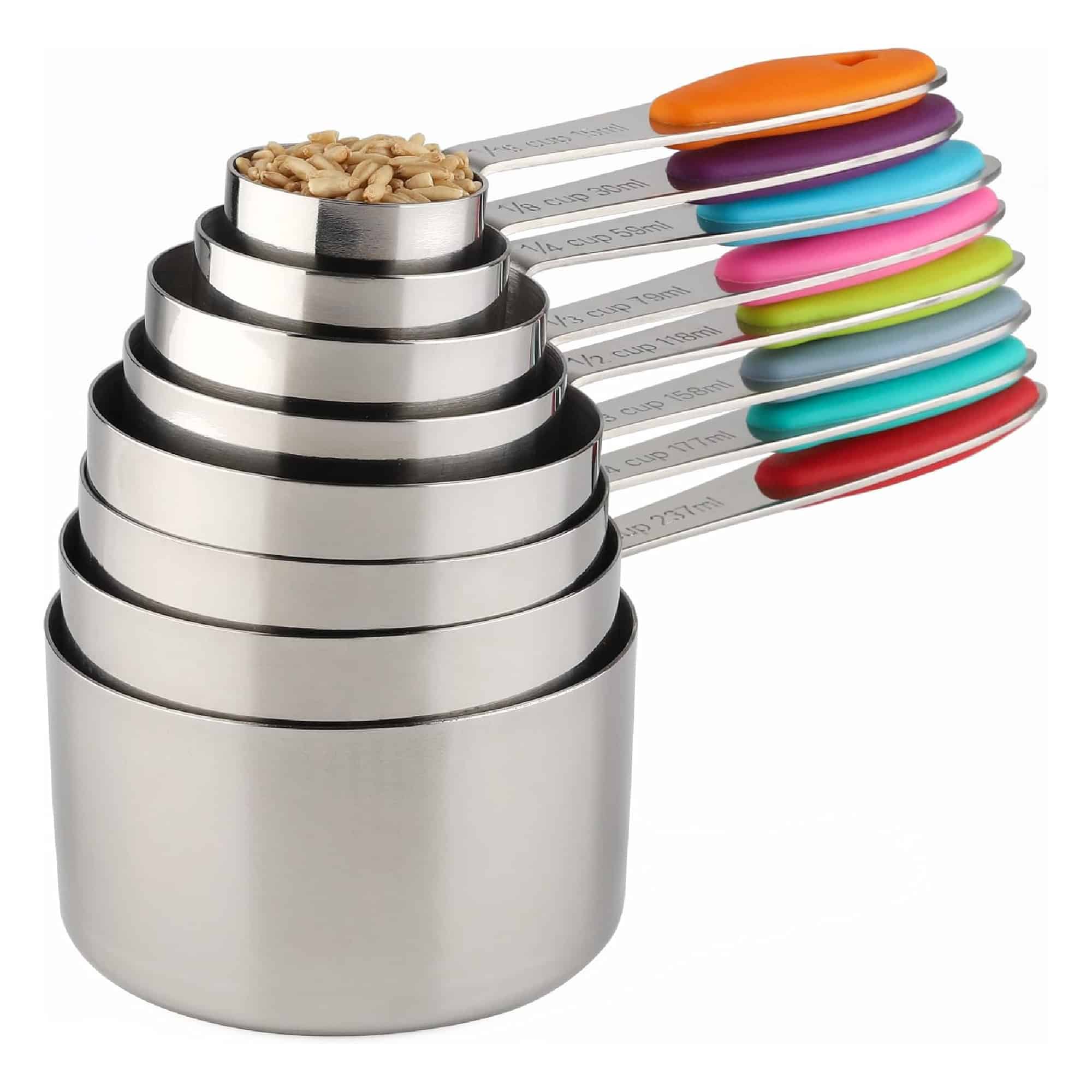 Set of seven stainless steel measuring cups stacked together, each with colorful handles. The top cup contains grains.