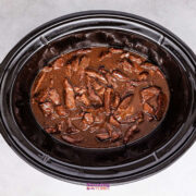 A slow cooker filled with tender chunks of beef and crisp broccoli, all enveloped in a rich, brown sauce, viewed from above on a light gray surface.