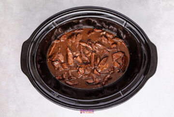 A slow cooker filled with tender chunks of beef and crisp broccoli, all enveloped in a rich, brown sauce, viewed from above on a light gray surface.