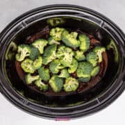 Succulent slow cooker beef nestled beneath tender broccoli florets, ready to delight your senses, all set atop a gray surface.