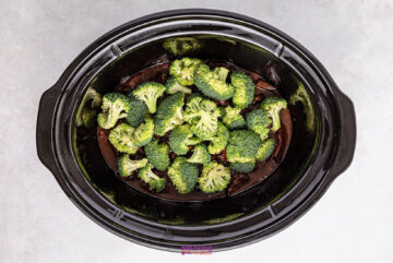 Succulent slow cooker beef nestled beneath tender broccoli florets, ready to delight your senses, all set atop a gray surface.