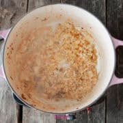 Chopped onions simmer in a pot with pink handles, preparing the base for a delicious calabrese pasta sauce on a rustic wooden surface.