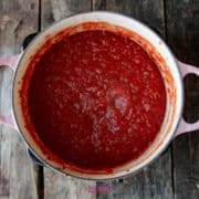 A pot filled with thick, red tomato sauce, perfect for a calabrese pasta dish, sits on a wooden surface.