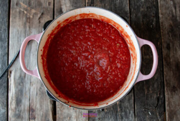 A pot filled with thick, red tomato sauce, perfect for a calabrese pasta dish, sits on a wooden surface.