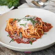 A plate of calabrese pasta with tomato sauce, garnished with grated cheese and chopped herbs, sits invitingly on a wooden table, complete with utensils and a napkin nearby.