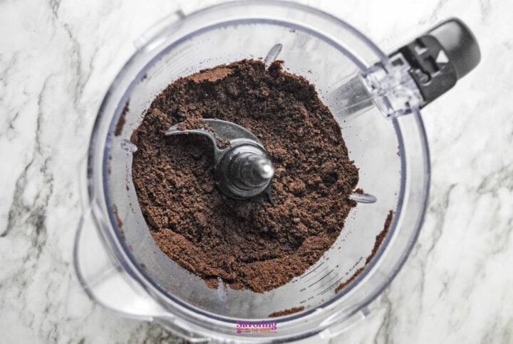 Ground chocolate powder in a food processor viewed from above on a marble surface.