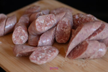 Sliced uncooked sausage pieces on a wooden cutting board.