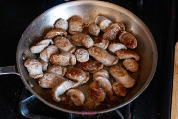 Sliced sausages cooking in a stainless steel pan on a stove.