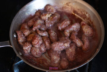 Chunks of meat cooking in a pan with a red liquid.
