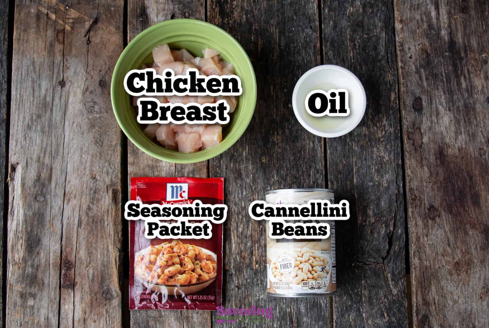 A green bowl of diced chicken breast, a can of cannellini beans, and a small bowl of oil are perfectly staged alongside a McCormick White Chicken Chili seasoning packet on a wooden surface.