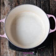 Empty pink-handled pot on an electric stove set on a wooden surface, with a partially visible packet on the left side.