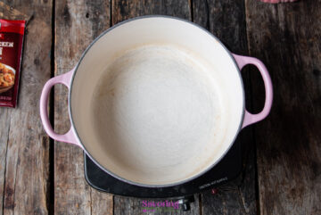 Empty pink-handled pot on an electric stove set on a wooden surface, with a partially visible packet on the left side.