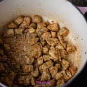 Cubed chicken pieces seasoned with spices are cooked in a large, pink-handled pot, set on a wooden surface.