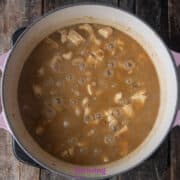A pot of chicken and dumplings with McCormick white chicken chili seasoning simmers on a wooden surface, with chunks of chicken nestled in the rich, aromatic brown broth.