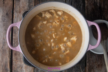 A pot of chicken and dumplings with McCormick white chicken chili seasoning simmers on a wooden surface, with chunks of chicken nestled in the rich, aromatic brown broth.