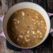 A pot of chicken and white bean chili simmering on the stovetop, filled with chunks of chicken and beans in a seasoned McCormick White Chicken Chili broth. The pot boasts vibrant pink handles.
