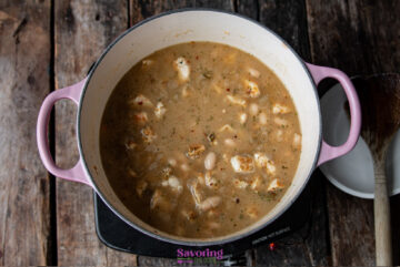 A pot of chicken and white bean chili simmering on the stovetop, filled with chunks of chicken and beans in a seasoned McCormick White Chicken Chili broth. The pot boasts vibrant pink handles.