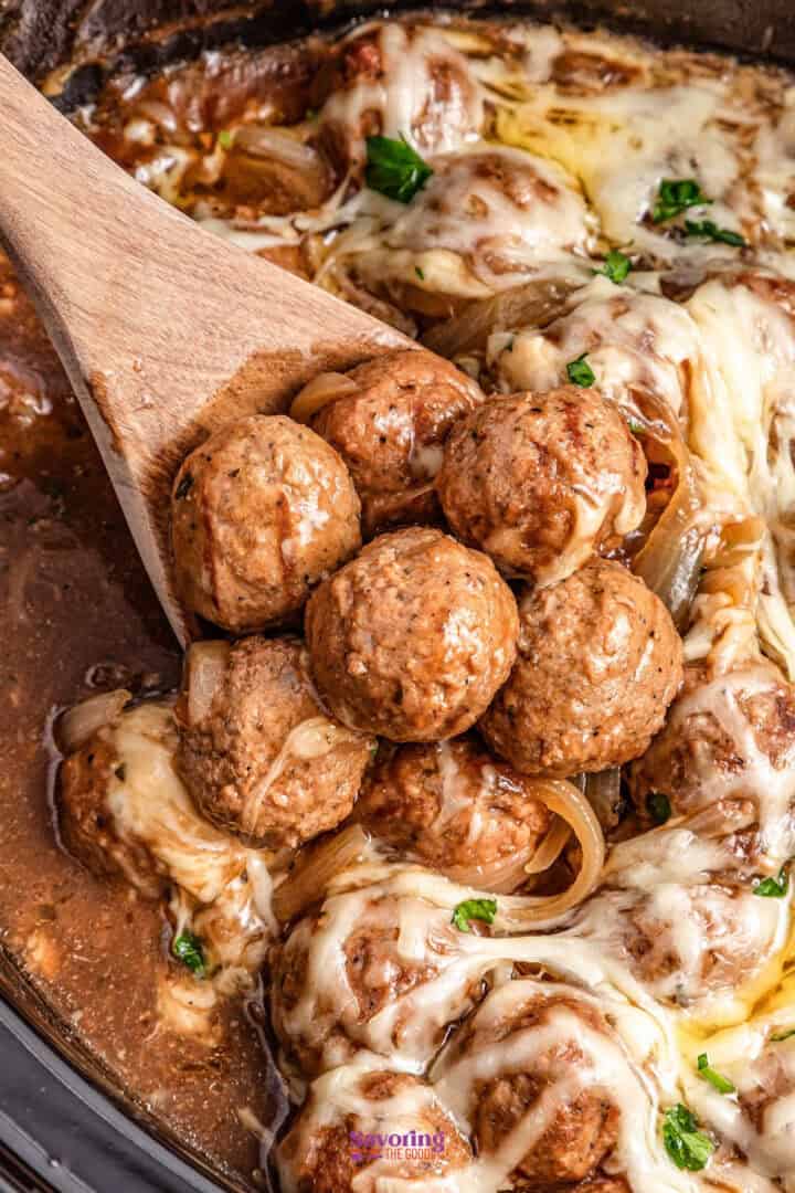 Meatballs covered in melted cheese and sauce in a pan, with a wooden spoon lifting a portion.