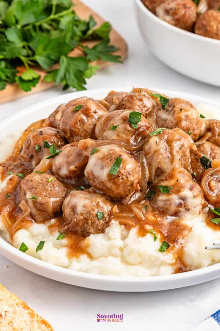 A plate of meatballs in brown gravy on top of mashed potatoes, garnished with parsley.