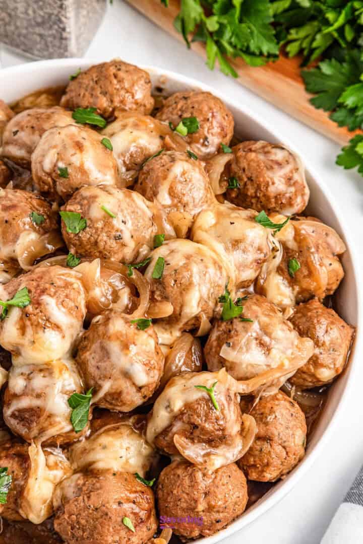 A bowl of glazed meatballs topped with melted cheese and garnished with parsley.