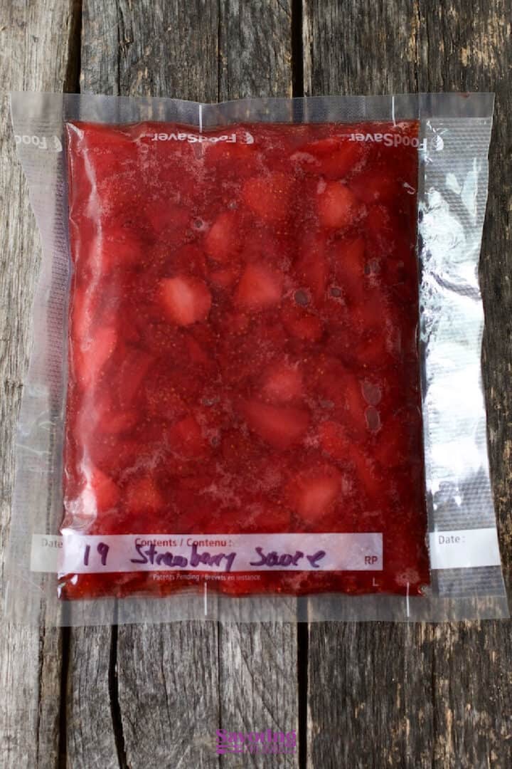 A sealed vacuum bag filled with strawberry sauce, labeled with a date, on a wooden surface.