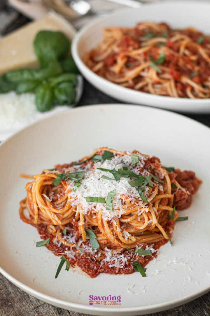 A plate of calabrese pasta with marinara sauce, topped with grated cheese and herbs. Another plate is seen in the background.