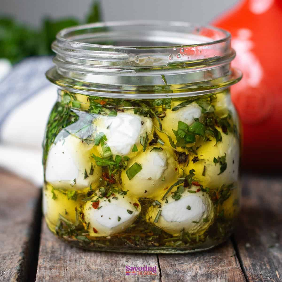 A jar filled with marinated mozzarella balls in olive oil, herbs, and spices, placed on a rustic wooden surface.