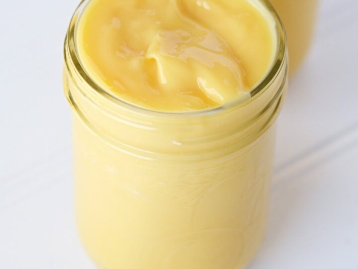 A glass jar filled with smooth, yellow sous vide lemon curd sits on a white surface.