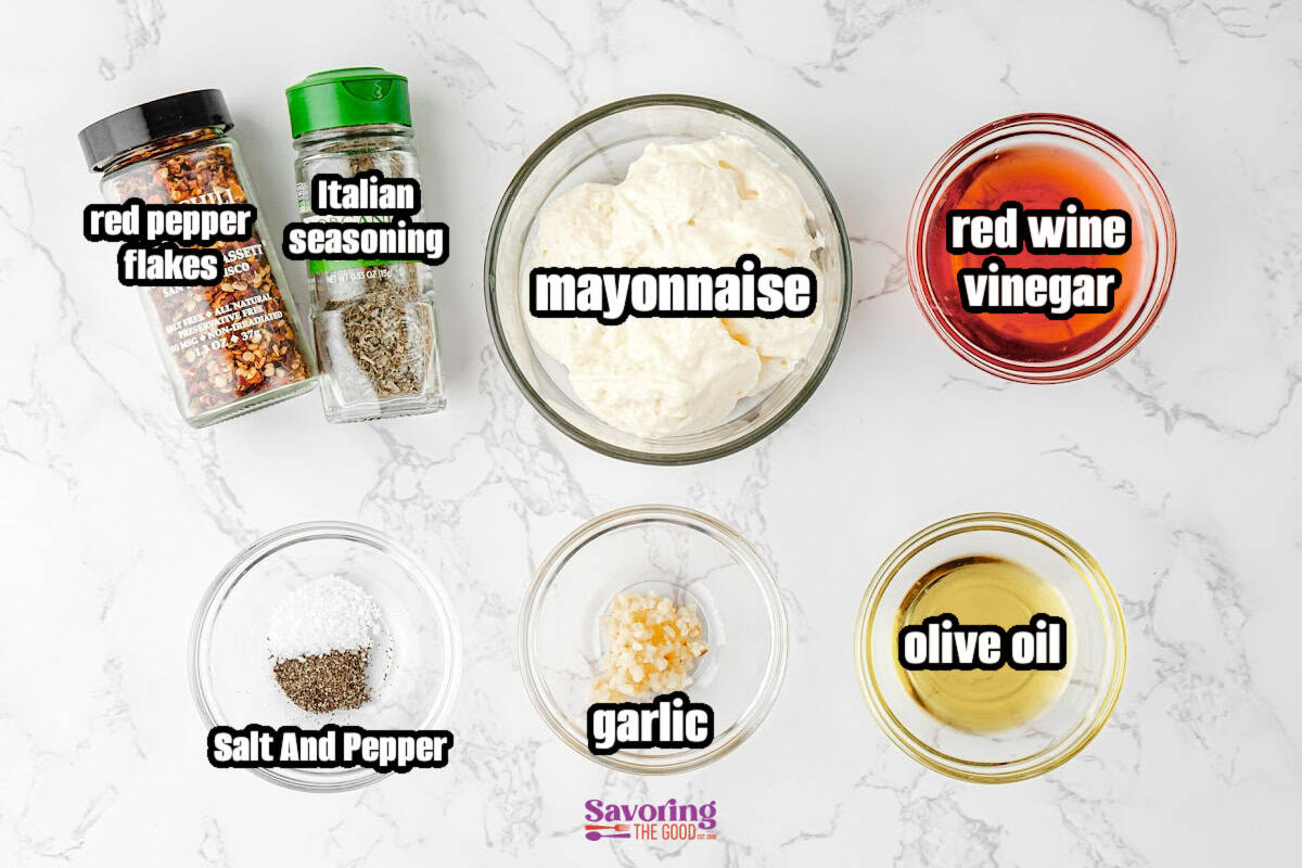 Overhead view of labeled ingredients in bowls and jars: mayonnaise, red wine vinegar, olive oil, garlic, salt and pepper, Italian seasoning, and red pepper flakes.