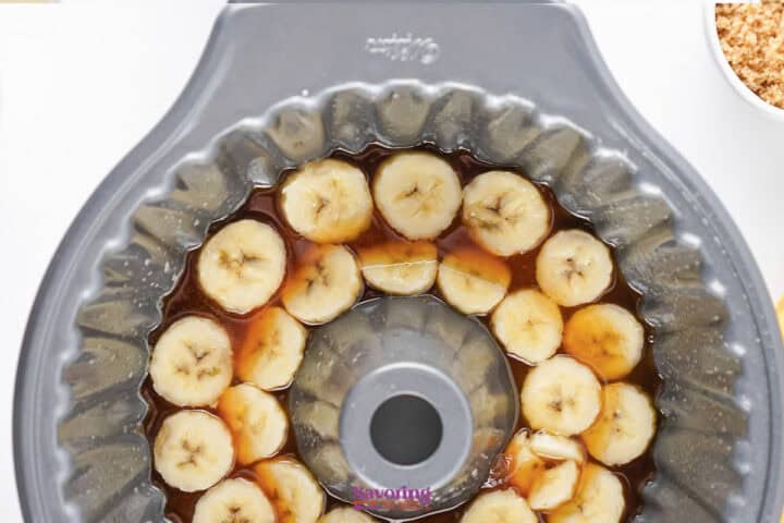 Sliced bananas arranged in a bundt pan with caramel sauce, ready to be baked.