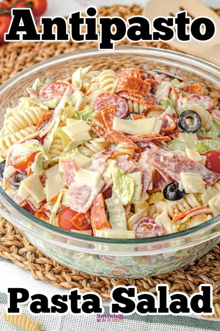 A glass bowl filled with antipasto pasta salad, containing rotini pasta, sliced meats, cheese, olives, tomatoes, and lettuce.