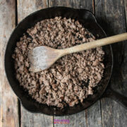 Cooked ground beef in a cast iron skillet with a wooden spoon, ready for your next chili pie Fritos creation, placed on a rustic wooden surface.