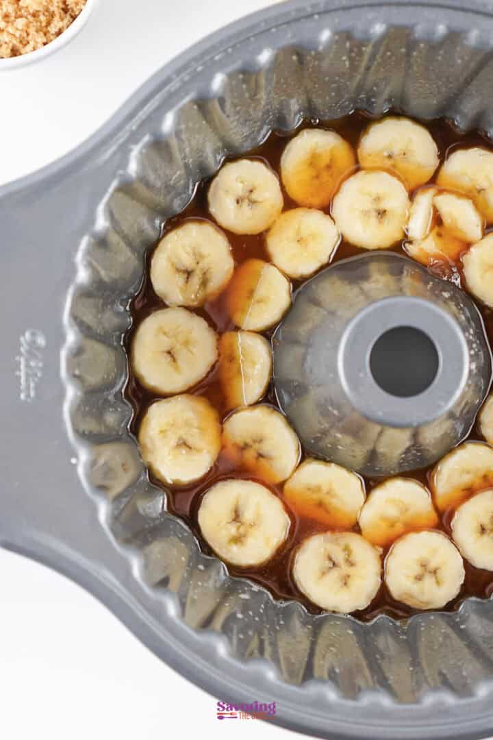 Sliced bananas arranged in a bundt pan with a brown syrupy liquid.