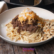 A plate of spaghetti topped with chili, shredded cheese, and diced onions, served with oyster crackers on the side.