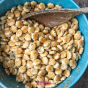 A blue bowl filled with seasoned oyster crackers being mixed with a wooden spoon on a wooden surface.
