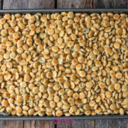 A baking sheet filled with seasoned oyster crackers spread out evenly on a wooden surface.