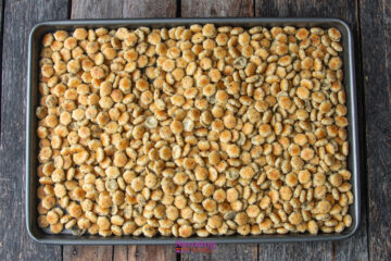 A baking sheet filled with seasoned oyster crackers spread out evenly on a wooden surface.