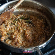 Chopped onions and herbs sautéing and browning in a stainless steel pan with a wooden spoon on a stovetop.
