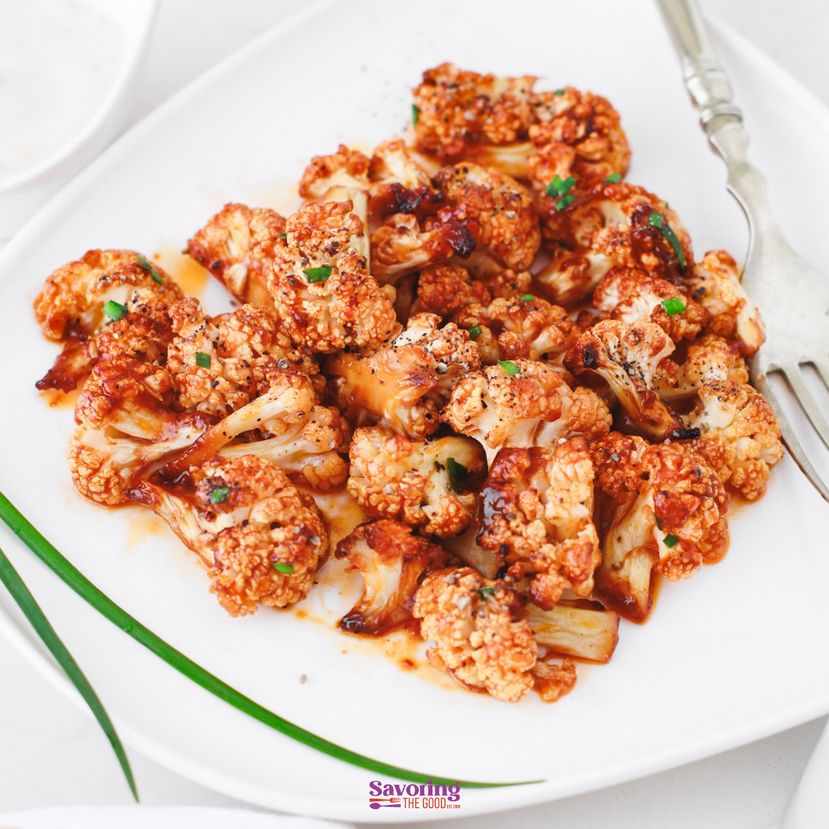 Buffalo cauliflower bites are roasted florets coated in a tangy red sauce, served on a white plate with a fork and garnished with fresh herbs.