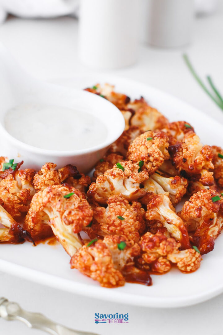 A plate of buffalo cauliflower bites garnished with herbs, served with a side of creamy dipping sauce.