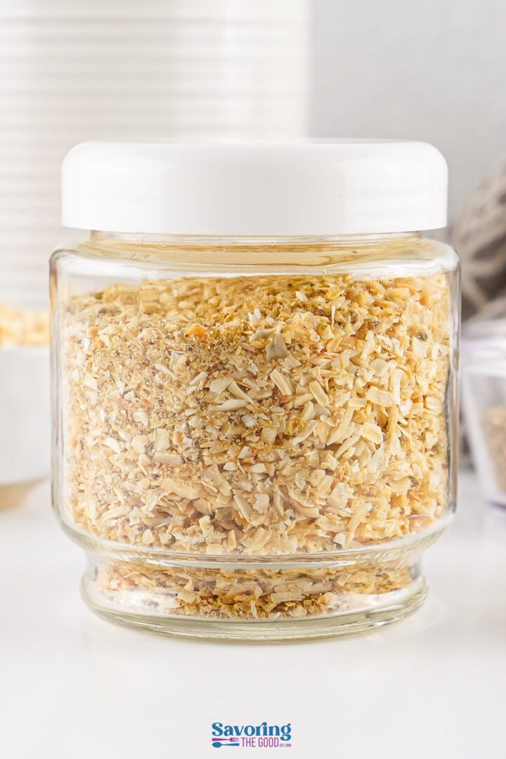 A glass jar with a white lid filled with dried minced onions sits on a white surface.