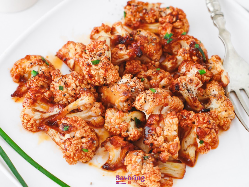 Roasted buffalo cauliflower florets coated in a spicy red sauce, served on a white plate with a fork on the side.