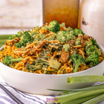 Beef lo mein: A white bowl filled with stir-fried noodles, beef, broccoli, and sliced green onions, garnished with sesame seeds, sits on a striped cloth with green onions nearby.