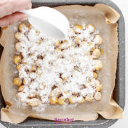 A hand sprinkles ranch dressing powder over a square baking dish lined with parchment paper and filled with chickpeas.