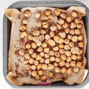 A baking tray lined with parchment paper holds a single layer of roasted and seasoned chickpeas.