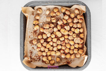 A baking tray lined with parchment paper holds a single layer of roasted and seasoned chickpeas.