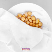 A white bowl lined with paper towels holding a portion of chickpeas, viewed from above on a light surface.