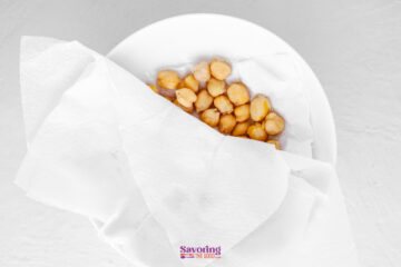 A white bowl lined with paper towels holding a portion of chickpeas, viewed from above on a light surface.