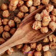 Close-up of roasted chickpeas coated in seasoning on parchment paper, with a wooden spoon scooping some up.